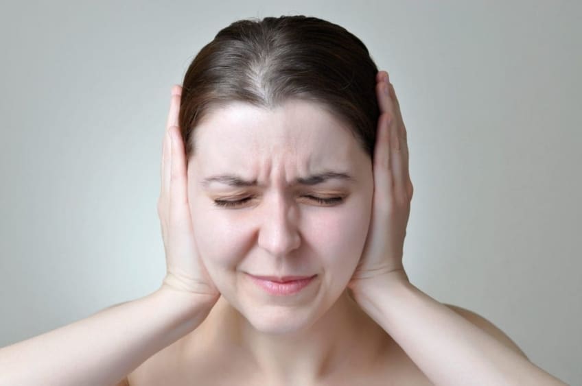 A young woman suffering from Meniere’s disease covers her ears and squeezes her eyes shut.